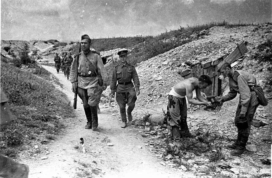 В расположении советских войск — подразделение на марше, умывание, блиндажи. Крым. Боец справа одет в летний камуфлированный маскировочный костюм зеленого цвета с хаотично расположенными черными амебообразными пятнами. 1944 г. Автор: Евгений Халдей.